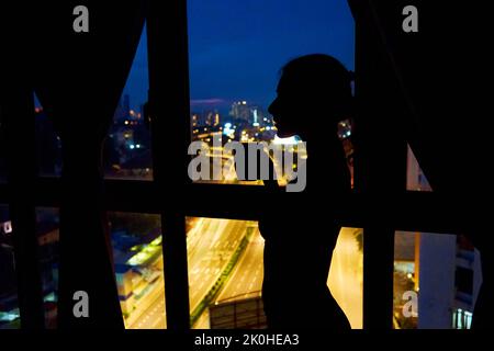 The silhouette of a girl against a stained-glass window looks at the night city. Stock Photo