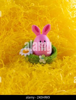 A Closeup of cute pink Easter Egg bunny inside green nest surrounded with bright yellow Stock Photo