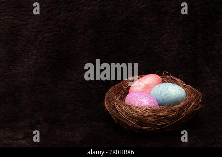 A Woven stick nest filled with speckled pink and blue eggs isolated on black background Stock Photo