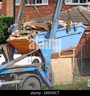 Full builders rubbish bin lifted from compact bungalow building construction site onto skip lorry truck for carting away to landfill site England UK Stock Photo