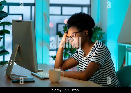 African American woman in glasses sits looking at monitor of computer working freelancer at home Stock Photo