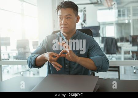 Asian businessman using sign language with colleagues and friends while sitting in office Stock Photo
