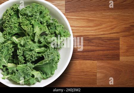 Chopped kale leaves in a white bowl shot from above on wooden table Stock Photo