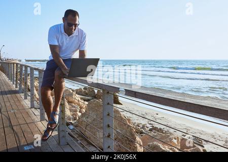 man working on laptop remotely from the beach Stock Photo