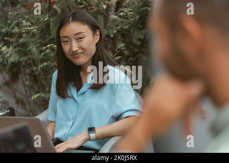 Smiling asian businesswoman working on computer sitting in coworking on colleagues background Stock Photo