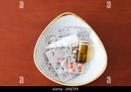 Many pills, drops in the nose, packages and blisters with pills lie in a plate on the table. Healthcare, medical industry. Healthy lifestyle Stock Photo