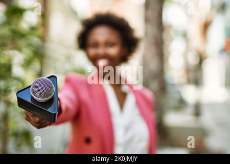 Young african american woman journalist pointing reporter microphone to the camera for television news Stock Photo