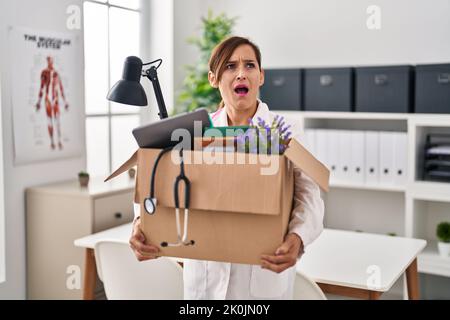 Middle age doctor woman holding cardboard box with items at the clinic angry and mad screaming frustrated and furious, shouting with anger. rage and a Stock Photo