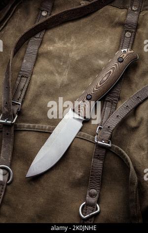 A hunting knife with a wooden handle on a khaki canvas backpack. Weapons for self-defense and survival. Stock Photo