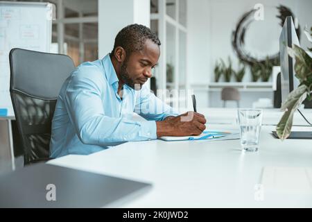Confident African businessman taking notes while sitting in modern office Stock Photo