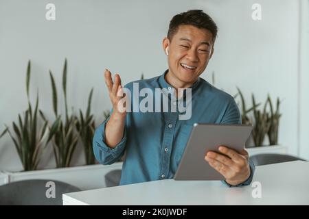Smiling asian businessman making videocall to client sitting in modern coworking Stock Photo