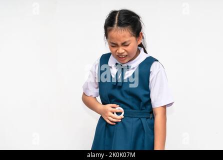 Little Asian student girl is stomach ache, unidentified school uniform, isolated portrait of Asian child girl with stomach pain on white background. Stock Photo