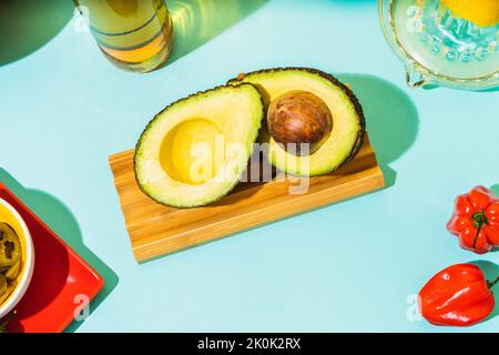 Top view of halved ripe avocado placed on lumber board near habanero pepper on blue background Stock Photo