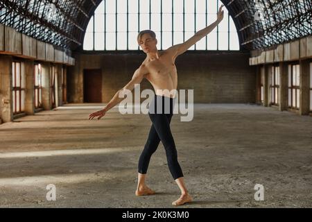 Flexible young ballet dancer in leotard training in large empty hall Stock Photo