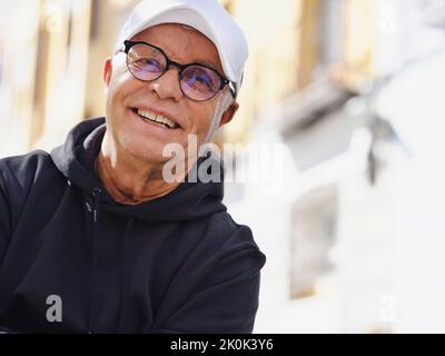 Handsome elderly male in trendy eyeglasses and stylish wear looking at camera on blurred background of street Stock Photo