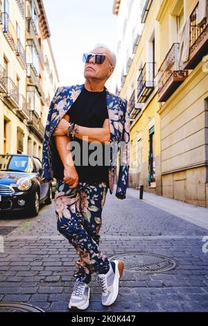 Trendy senior wearing stylish suit with floral print standing in the street looking away while posing Stock Photo