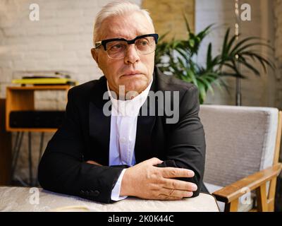 Elderly male in casual wear sitting at table in cozy cafeteria and looking away Stock Photo