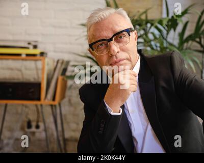 Elderly male in casual wear sitting at table in cozy cafeteria and looking at camera Stock Photo