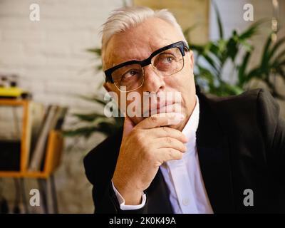 Elderly male in casual wear sitting at table in cozy cafeteria and looking away Stock Photo