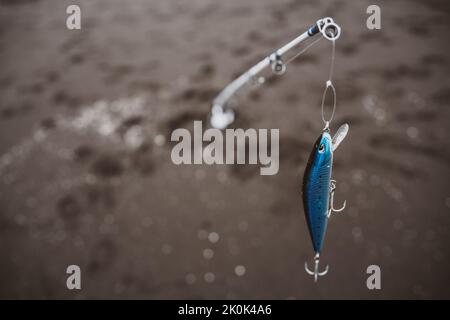 From above of long fishing pole with blue plug and guide rings hanging on line placed in rippling water of sea Stock Photo