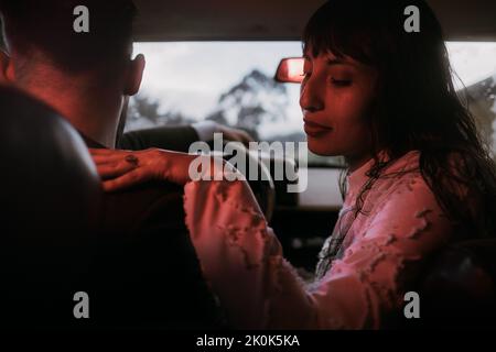 Loving bride and groom in stylish clothes sitting in car with red neon illumination on wedding day Stock Photo