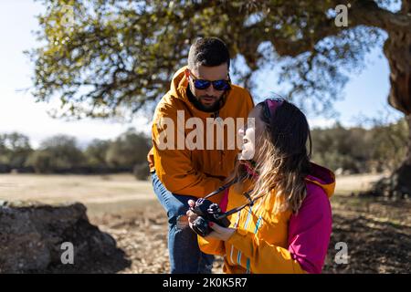 Young woman and boyfriend taking picture of nature landscape with professional camera while hiking outdoors Stock Photo