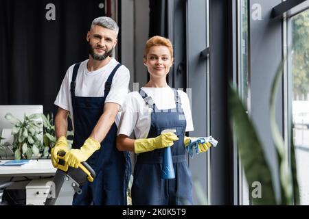 smiling professional cleaners in uniform looking at camera in office,stock image Stock Photo