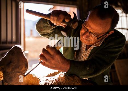 Senior woodworker in glasses using chisel and hammer while working with ...