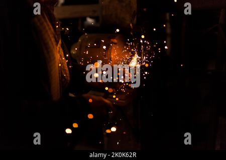 Unrecognizable elderly craftsman using bench grinder to shape metal part while working in dark workshop Stock Photo