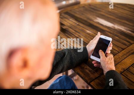 Elderly man using his smart phone sitting at the table in his house Stock Photo