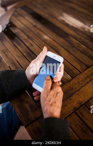 Elderly man using his smart phone sitting at the table in his house Stock Photo