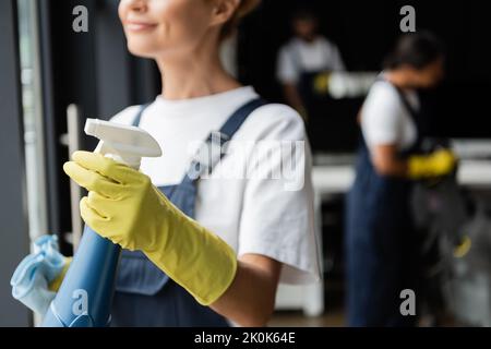 partial view of smiling woman in rubber glove holding spray bottle with detergent,stock image Stock Photo