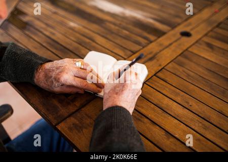 Elderly man writing in his notebook on the porch of his house Stock Photo