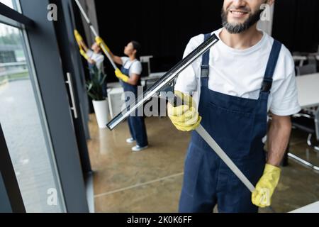 smiling man holding window squeegee near blurred interracial women,stock image Stock Photo