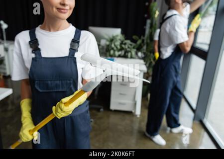 cropped view of blurred woman in overalls holding window squeegee near team working on blurred background,stock image Stock Photo