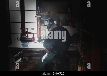 Back view of unrecognizable craftsman sitting working in dark workshop Stock Photo