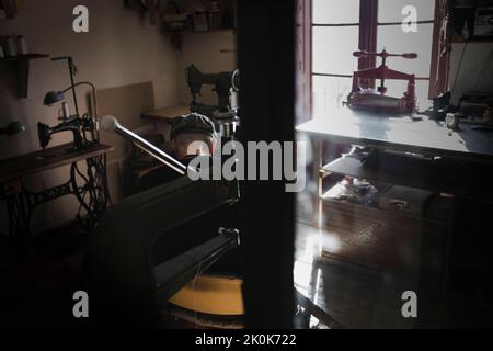 Back view of unrecognizable craftsman sitting working in dark workshop Stock Photo