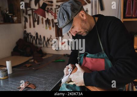 Craftsman in dark workshop cleaning leather bag Stock Photo