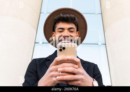 From below of young male in hat and formal wear browsing on cellphone in town Stock Photo