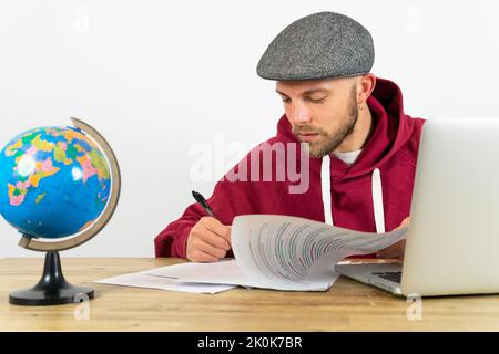 Concentrated male employee with pen working with papers at desk with laptop and small globe during work in modern office Stock Photo