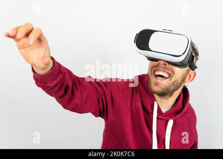 Joyful male in modern VR goggles smiling while exploring virtual reality with outstretched arm against white background in light studio Stock Photo