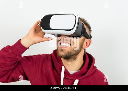 Joyful male in modern VR goggles smiling while exploring virtual reality against white background in light studio Stock Photo