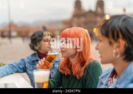 Side view of positive young female friends drinking beer while resting in outdoor pub in city of Cusco Stock Photo