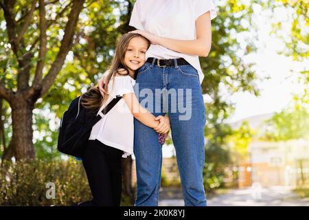 The daughter holds onto her mother's leg and smiles at the camera before leaving for school. Stock Photo