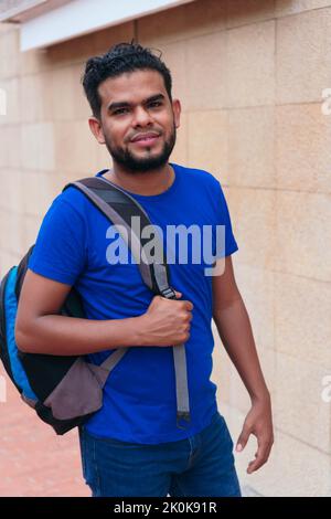 Positive ethnic male student with rucksack standing in city street and looking at camera Stock Photo