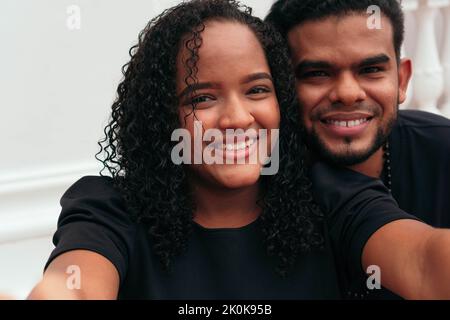 Delighted ethnic couple in black clothes taking self shot on mobile phone in city street Stock Photo
