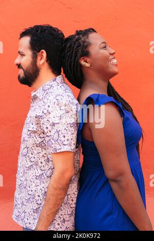 Side view of positive multiracial couple standing back to back on orange background in street Stock Photo
