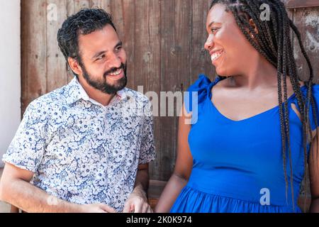 Delighted multiracial couple standing near wooden building in street and looking at each other Stock Photo