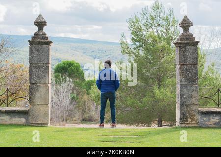 Back view of middle-aged man standing between a stone columns while pensively looking at the sky Stock Photo