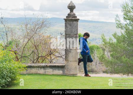 Middle-aged man leaning on a stone column while pensively looking at the sky Stock Photo